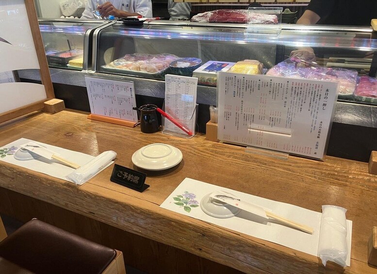 A sushi bar with a wooden counter, chopsticks, a plate, and a menu. 1