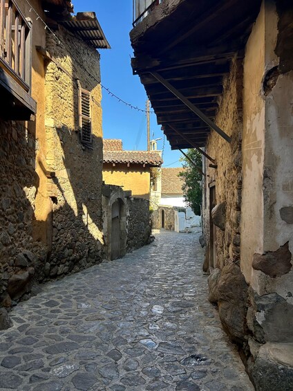 A narrow cobblestone street flanked by old stone buildings with wooden shutters and a tiled roof. 4