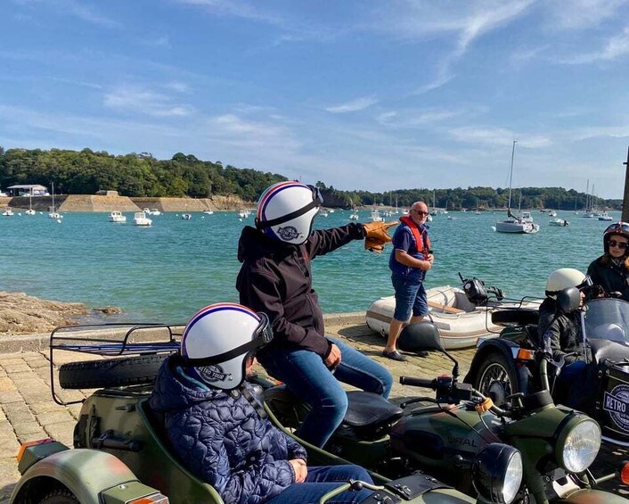 People on motorcycles and a boat near a body of water with boats in the background. 2