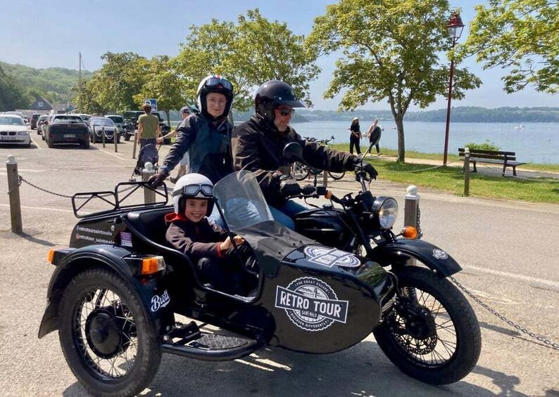 A retro tour motorcycle with a sidecar, parked by a lakeside path. 1