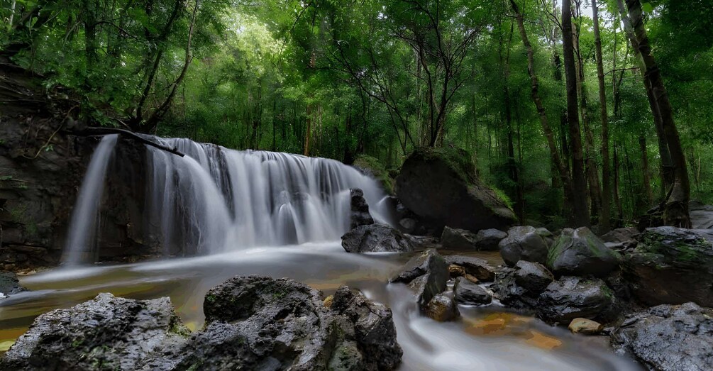 A waterfall in a forested area with rocks and a stream. 3