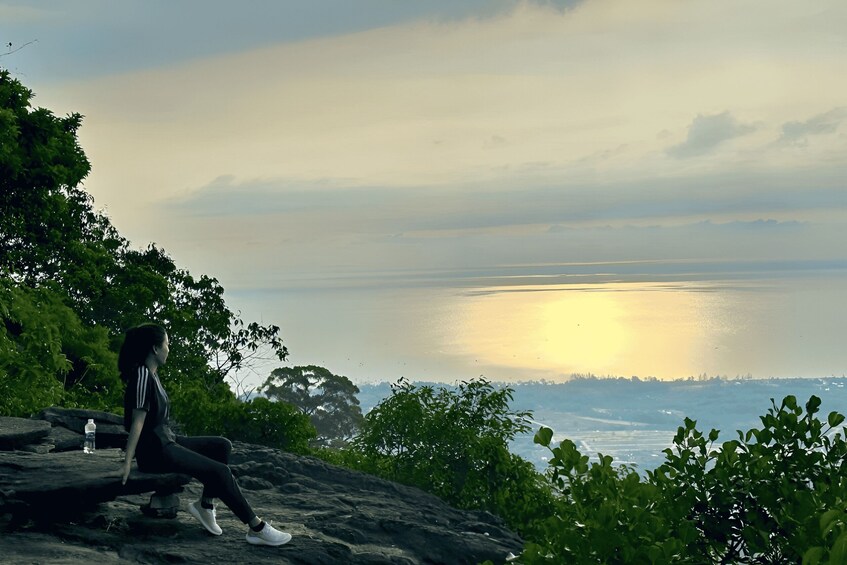 A person sitting on a rock overlooking a body of water with a sunset in the background. 2