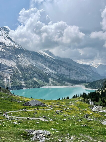 A mountain landscape with a turquoise lake, green fields, and snow-capped peaks. 2