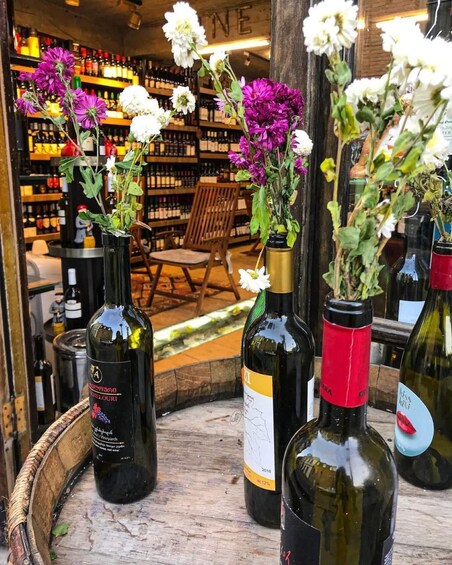 Wine bottles with flowers in front of a bar with shelves of bottles. 1