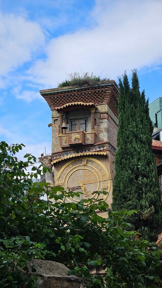 A clock tower with intricate brickwork and a large clock face, surrounded by greenery and trees. 4