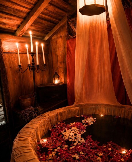A wooden room with a circular water feature surrounded by flowers, a candelabra with lit candles, and a hanging lantern. 5