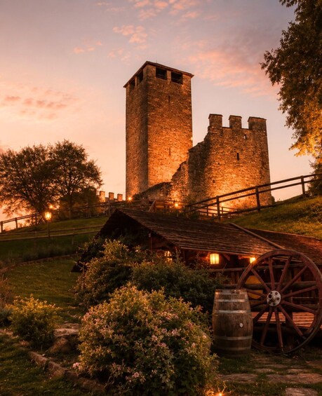 A historic stone tower and a wooden water wheel in a park setting. 2
