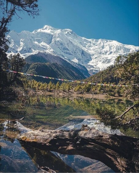 A mountain range with snow-capped peaks, a clear lake reflecting the scenery, and colorful prayer flags strung across the foreground. 3