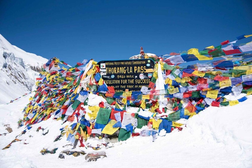 A sign at Thorong La Pass with colorful prayer flags. 1