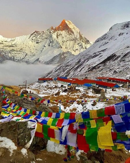 A snow-covered mountain with a prominent peak, colorful prayer flags, and a red-roofed building. 2
