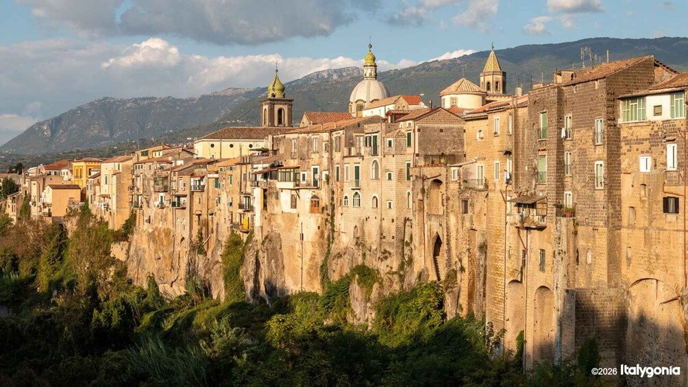 A historic town with terraced buildings, a church with a dome, and mountains in the background. 3