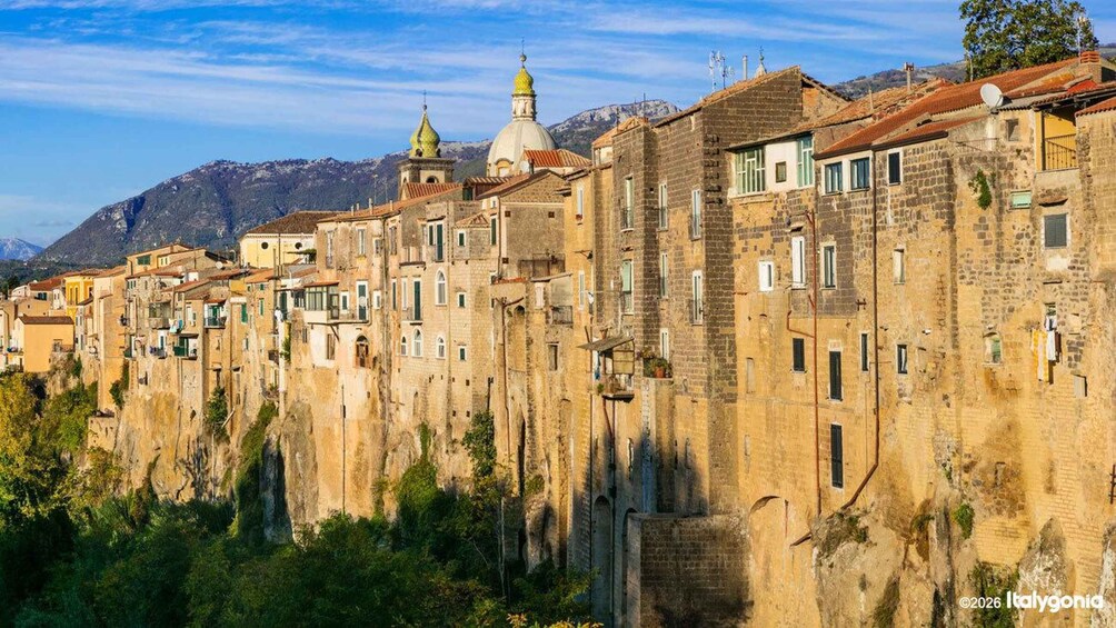A historic town with stone buildings, a church with a dome, and mountains in the background. 3