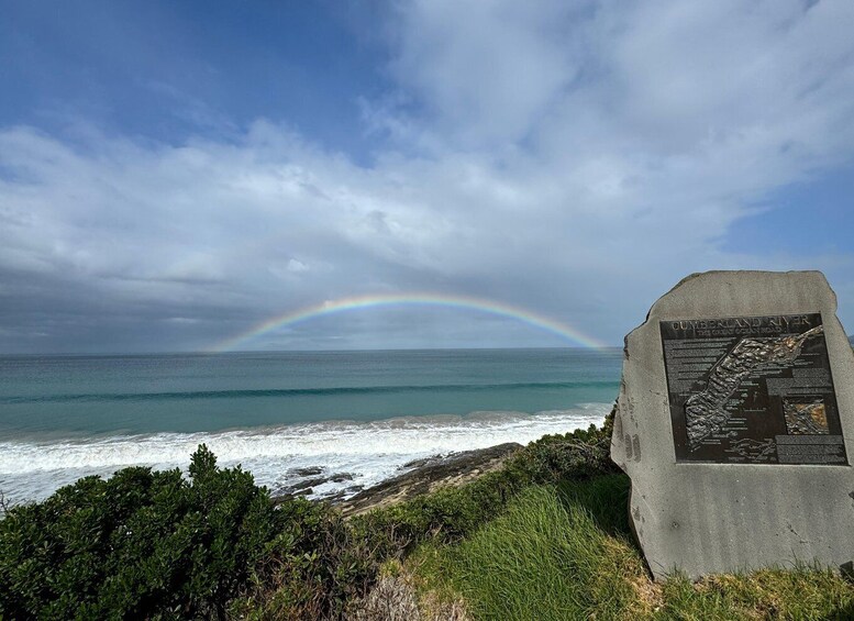 A coastal landscape with a stone monument, ocean waves, and a rainbow. 4