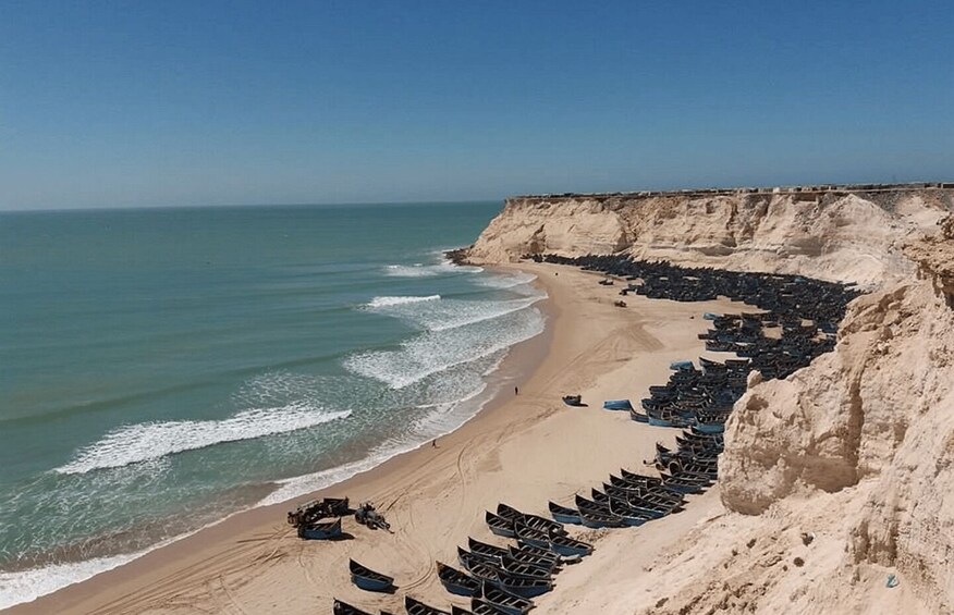 A beach with boats lined up on the shore and cliffs in the background. 2