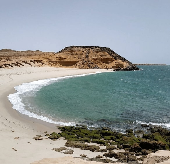 A sandy beach with a large rock formation and calm turquoise waters. 1