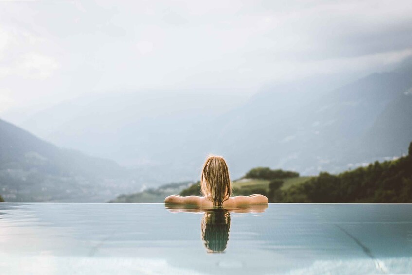 A person floating in a clear pool with a mountainous landscape in the background. 1