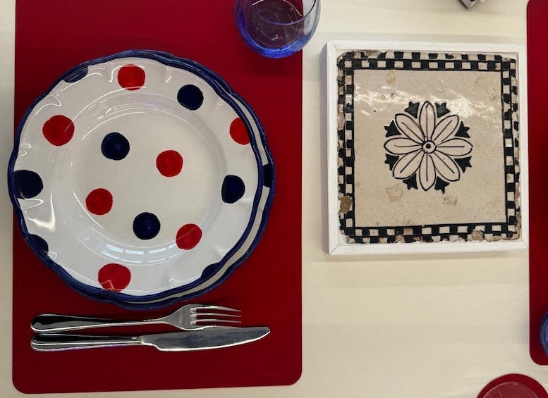 A red tablecloth with a white plate featuring red and blue polka dots, a silver fork, and a glass of blue liquid. 1