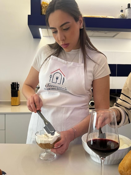 A person in a white apron with a logo, preparing a dessert in a glass bowl. 5