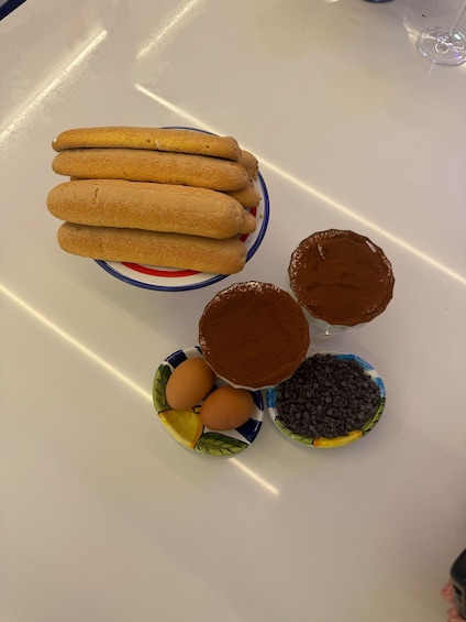 A plate with biscotti, a bowl of chocolate chips, a bowl of eggs, and a bowl of cocoa powder. 2