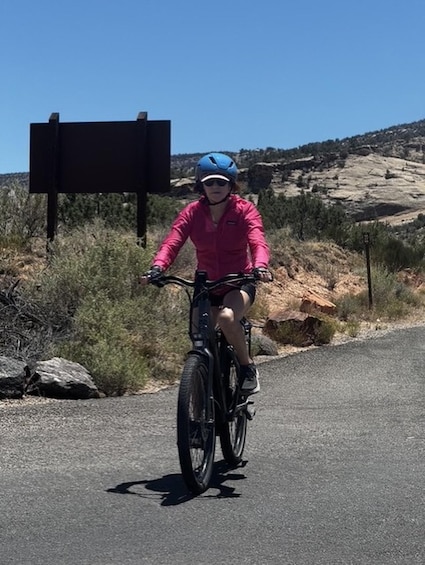 A person riding a bicycle on a road with a hilly landscape in the background. 3