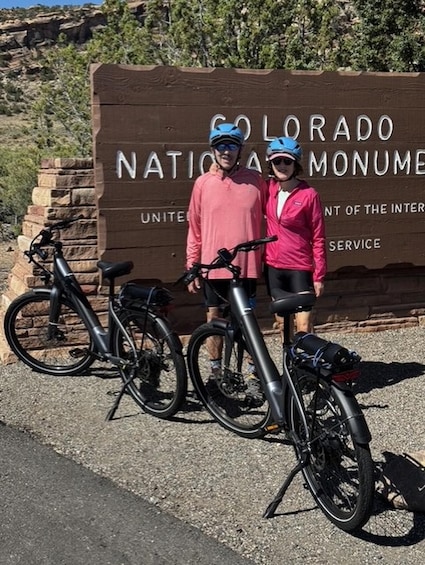 Two people standing in front of a sign for the Colorado National Monument. 1