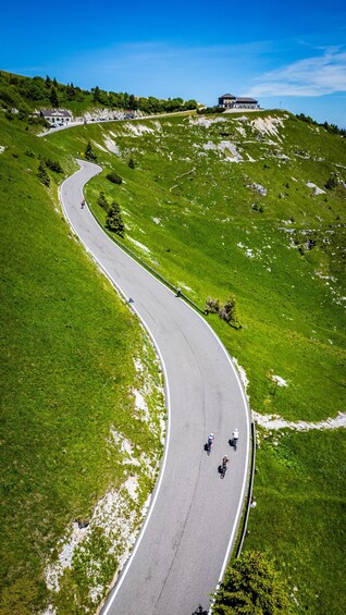 A winding mountain road with cyclists, a large building on a hill, and lush greenery. 1