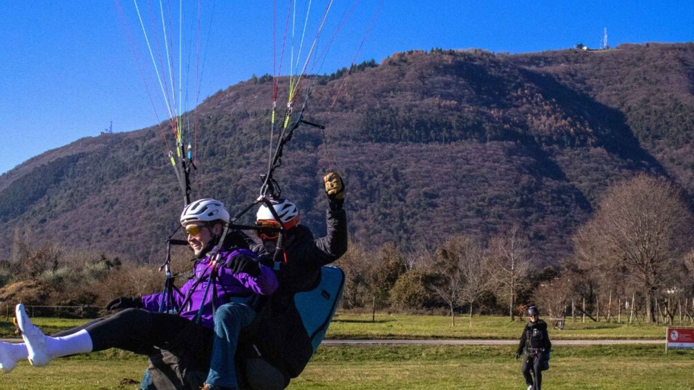 Two people on a tandem paragliding course with a hilly landscape in the background. 4