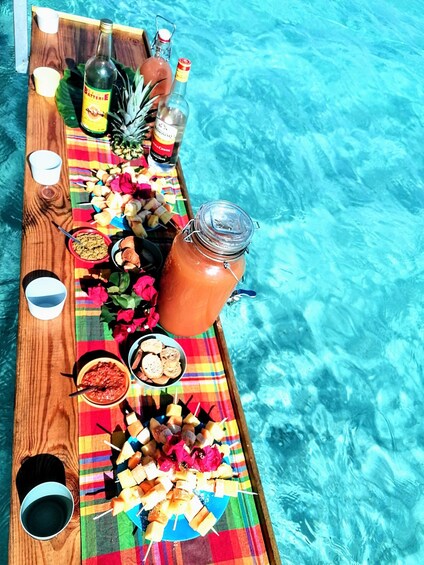A wooden tray with snacks, drinks, and a fruit platter by a pool. 1