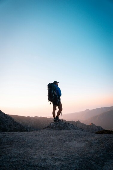 A hiker with a backpack on a rocky mountain peak during sunrise. 2