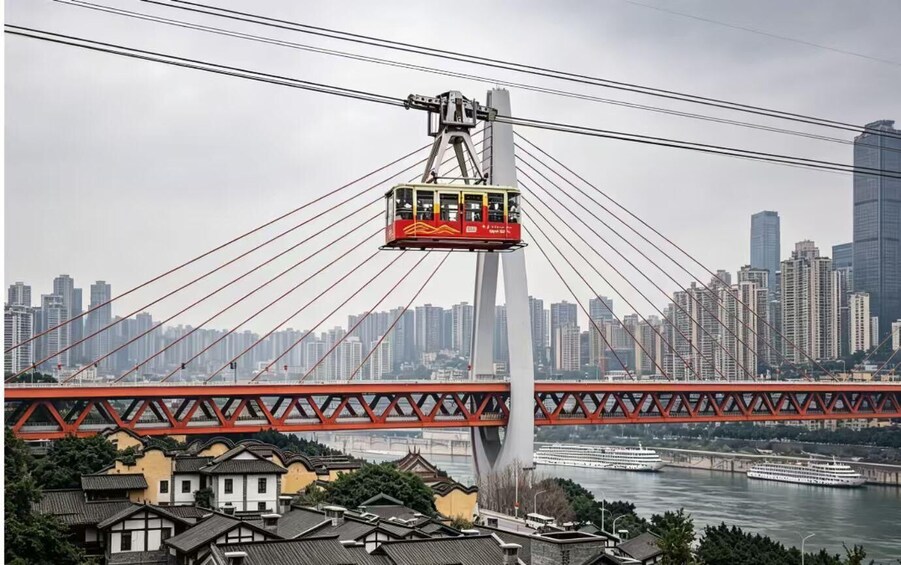 A cable car system with a red cable car suspended between two towers, a bridge with red trusses, and a river with boats. 1