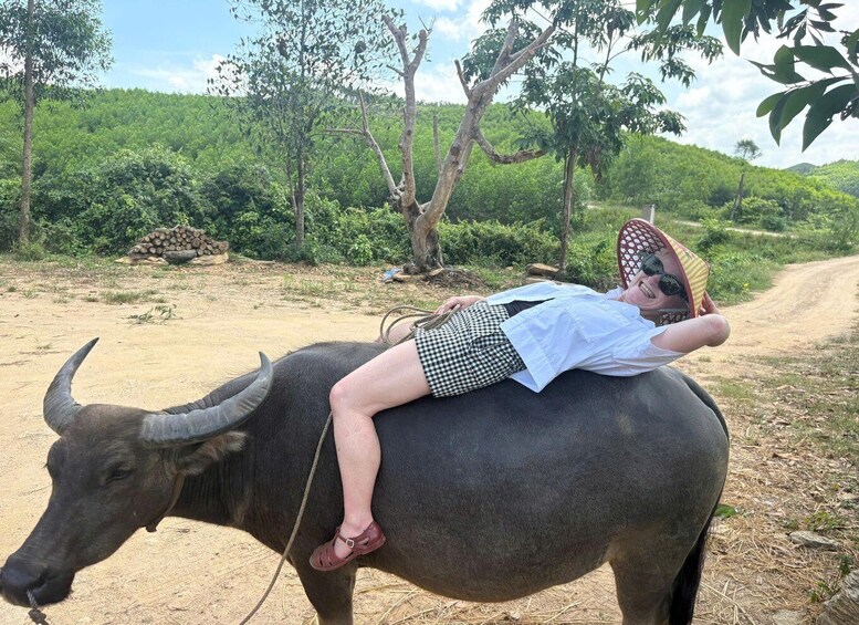 A person lying on a buffalo in a rural setting with greenery and a dirt path. 4
