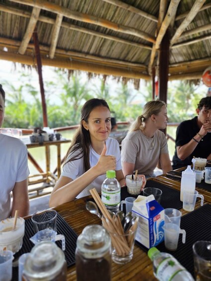 A group of people dining outdoors at a wooden table with various food and drink containers. 3