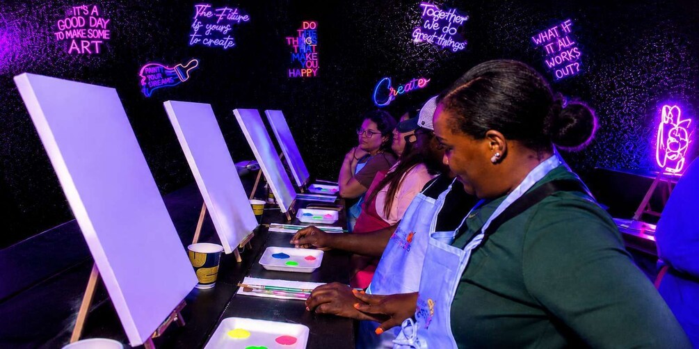 A group of people engaged in an art activity, with neon signs in the background. 1