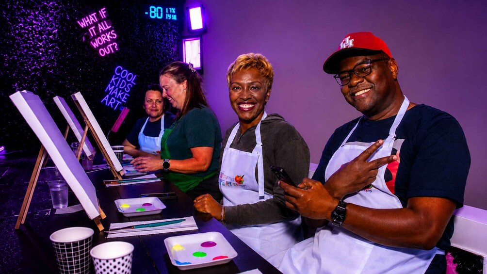 People at an art workshop with paint palettes and brushes, neon signs, and a digital clock. 3