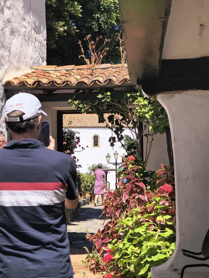A person in a striped shirt and white cap walking towards a white building with a tiled roof. 2