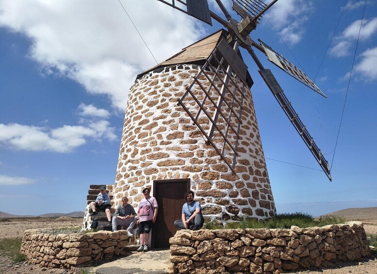 A stone windmill with people sitting in front of it. 1