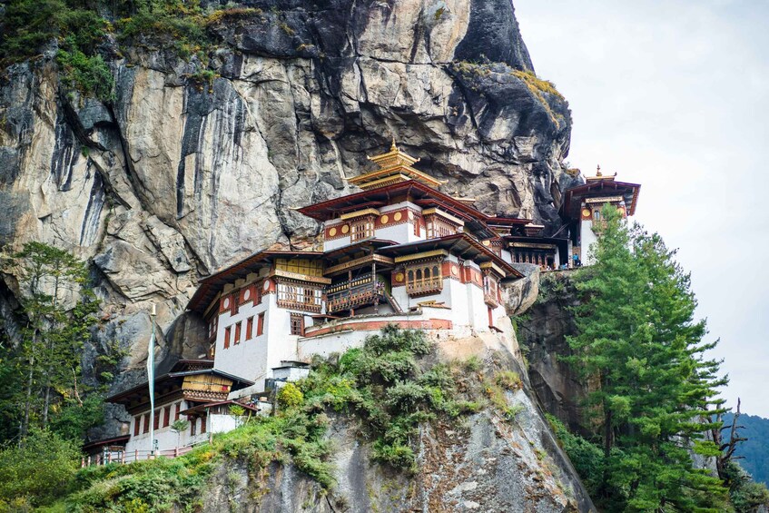 A traditional multi-tiered building perched on a cliffside, surrounded by lush greenery and rocky terrain. 1