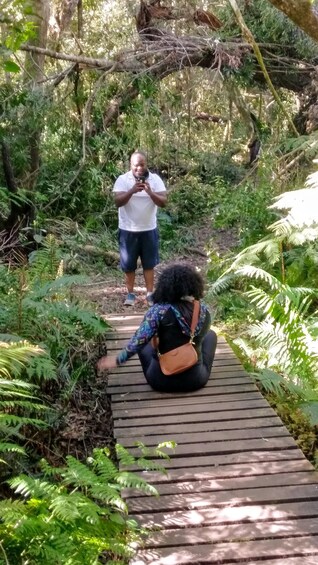 A person taking a photo on a wooden boardwalk surrounded by dense green foliage. 4