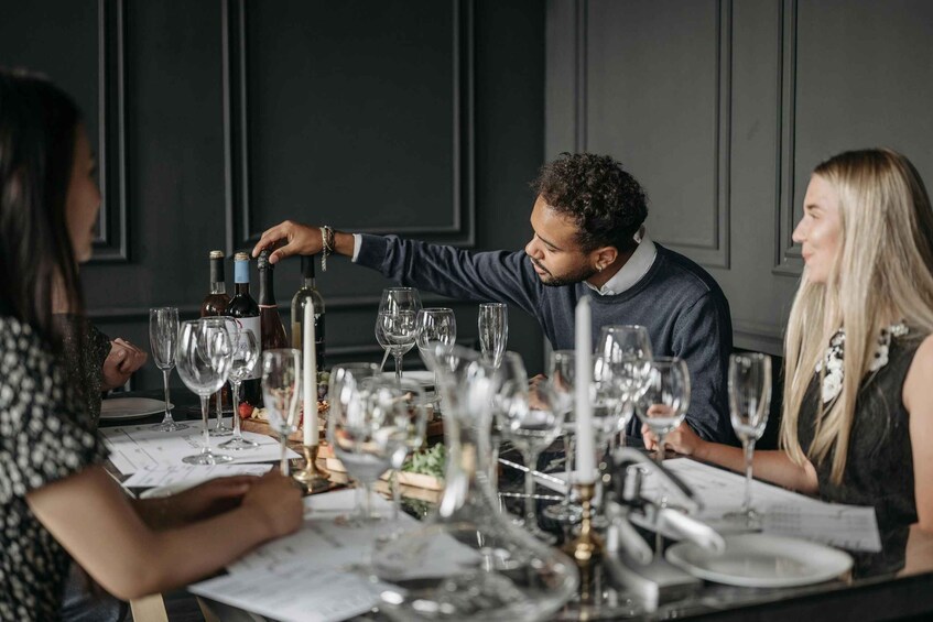 A group of people seated at a table with wine glasses and bottles, in a dimly lit room with dark walls. 1