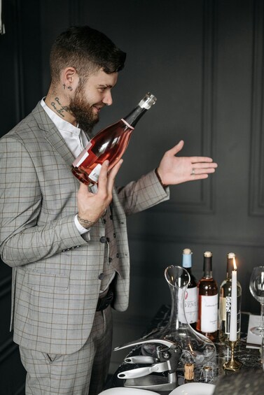 A person in a checkered suit holding a bottle, standing next to a table with various bottles and a candle. 2