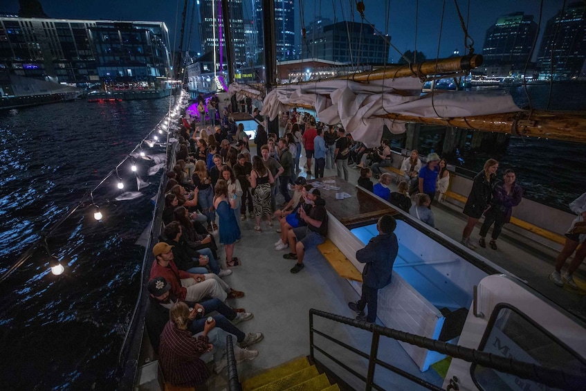 A nighttime boat tour with passengers on deck, city skyline in the background, and illuminated water. 1