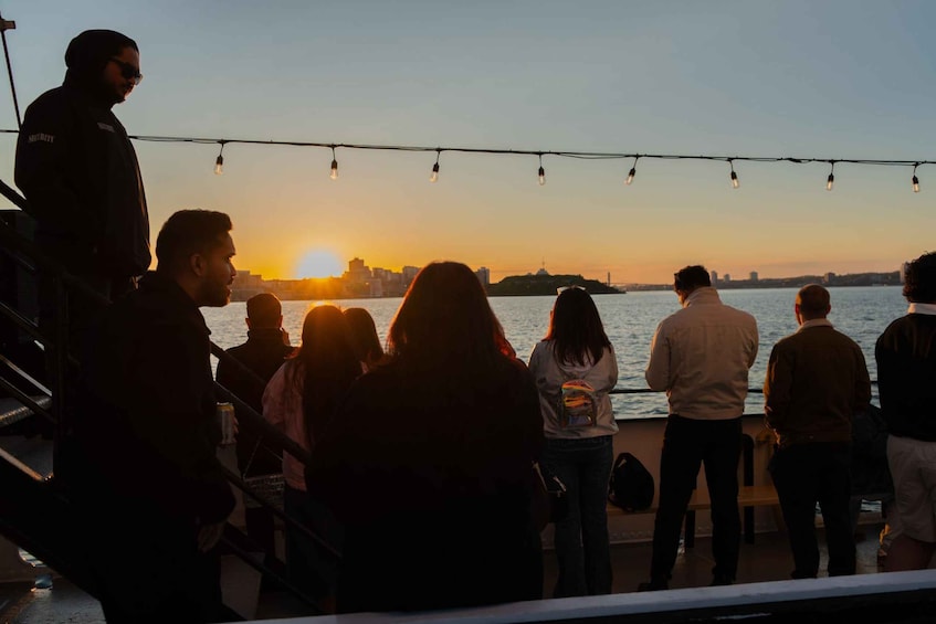 A group of people on a boat during sunset, overlooking a city skyline. 2