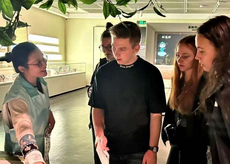 A group of people in an indoor setting with a glass display case and a plant overhead. 5