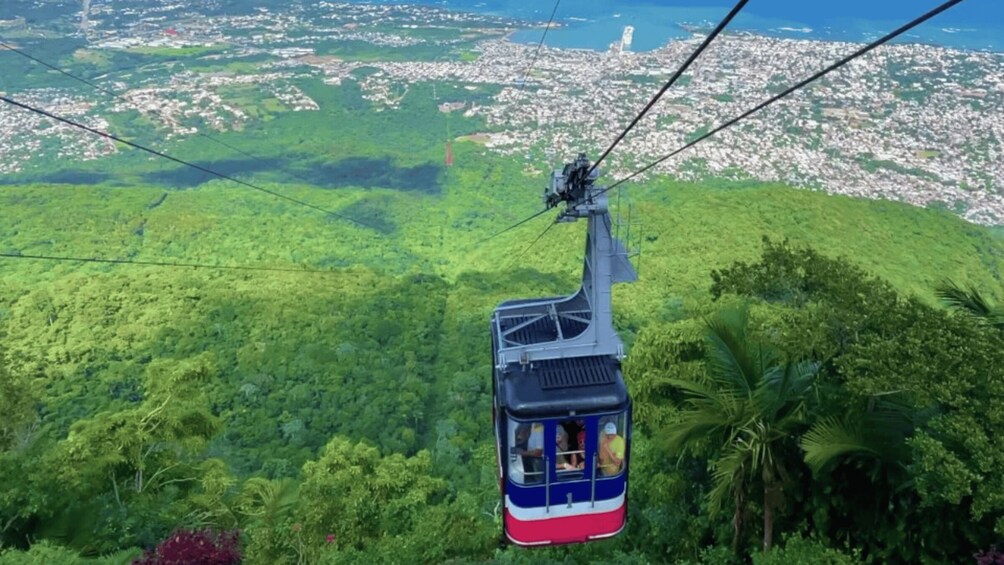 A cable car ascending a lush green mountain with a cityscape in the background. 2