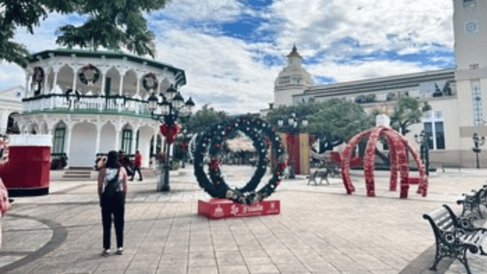 A plaza with a large circular wreath, a red sculpture, and a building with arches. 3