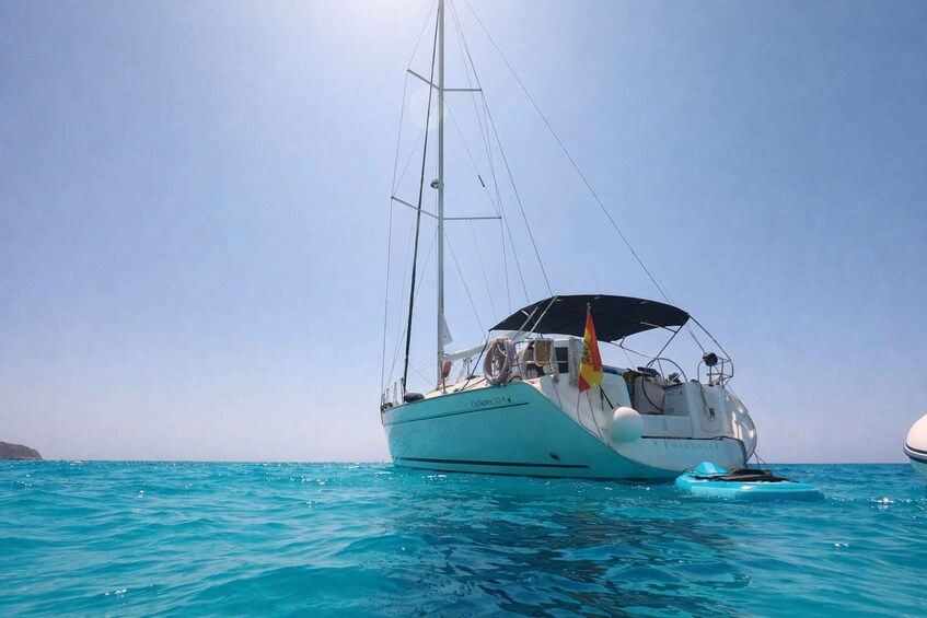 A sailboat named 'Olympos 504' with a blue canopy, anchored in clear turquoise waters. 2