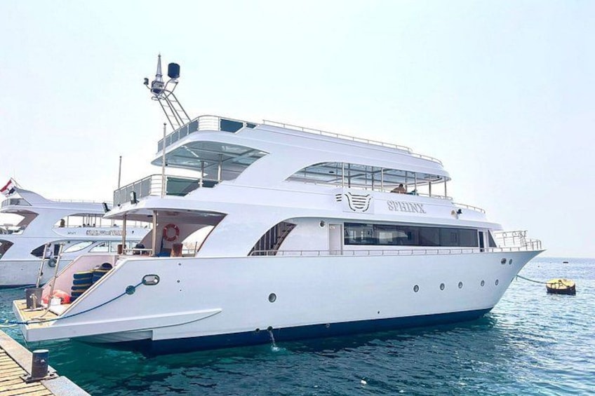 A large white yacht docked at a pier with multiple decks and a clear blue sky in the background. 1