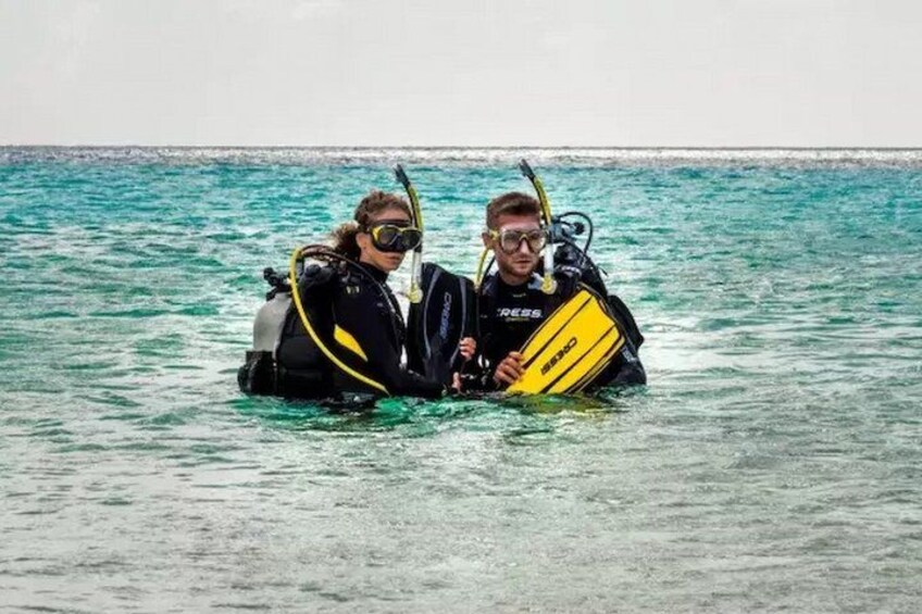 Two people in a body of water wearing scuba diving gear and holding a yellow diving board. 2