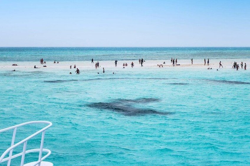 A beach with people swimming and walking, clear turquoise water, and a boat in the foreground. 4