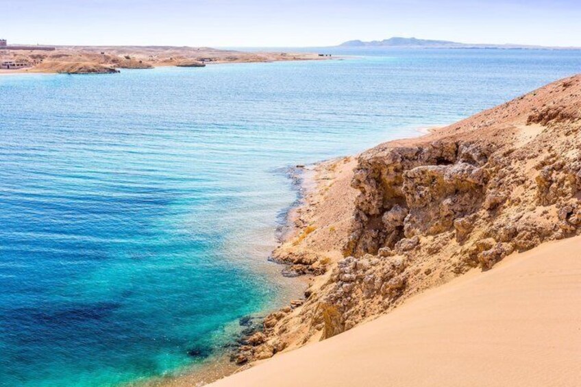A coastal landscape with clear blue waters, sandy beach, and rocky cliffs. 5